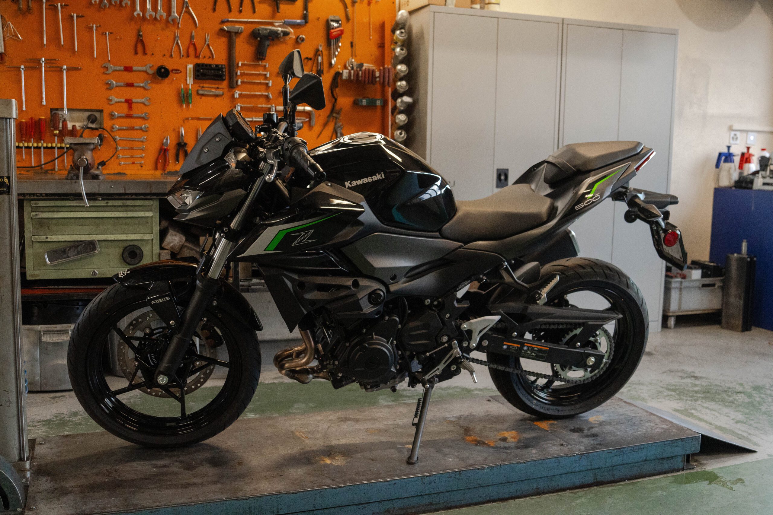 moto-kawasaki-z500-noire-et-verte-sur-plateforme-de-réparation-dans-atelier-pmh-motos-avec-outils-et-armoires-en-fond