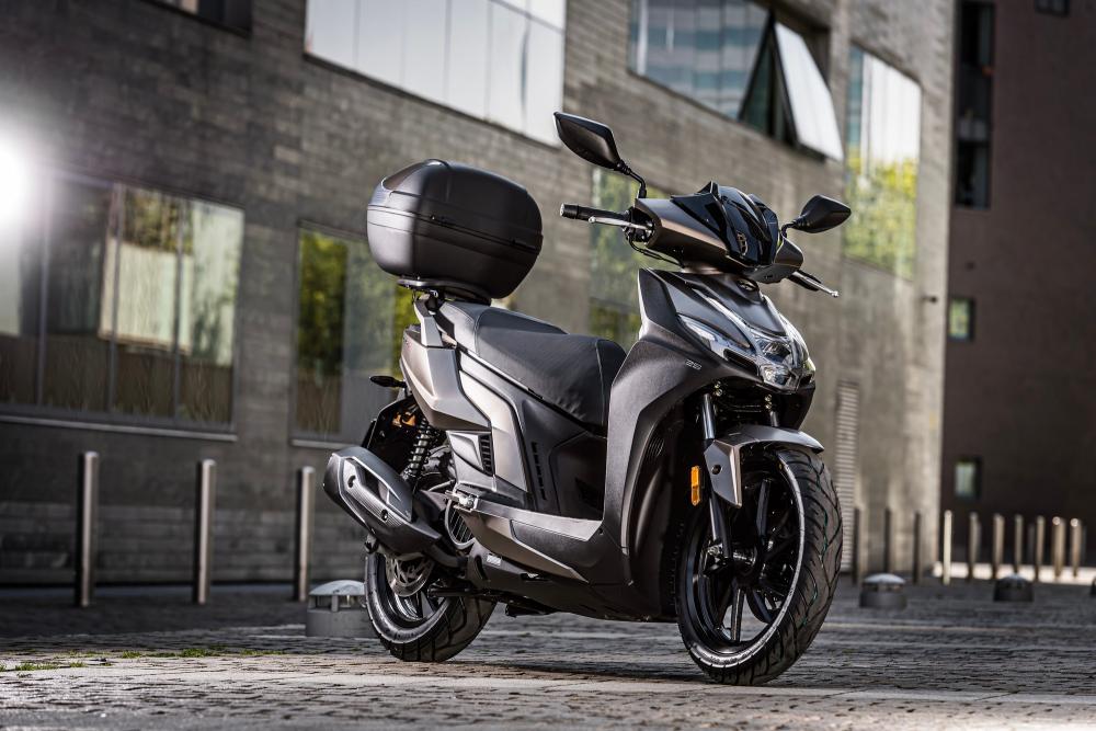 Scooter Kymco Agility S 125i gris avec top case photographié en environnement urbain vu trois quarts avant